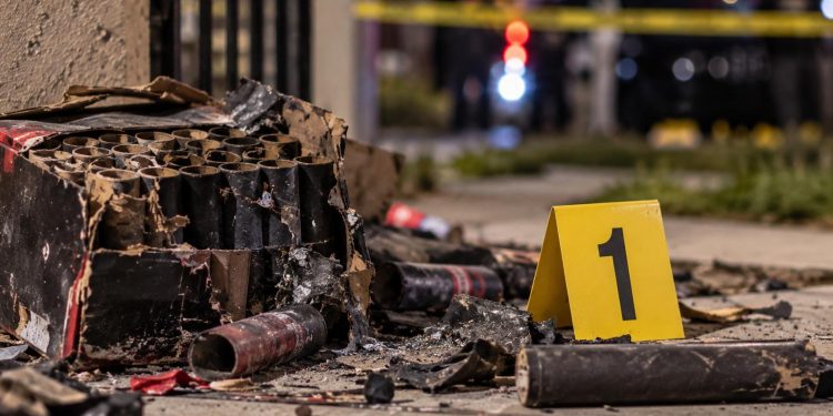 Close-up of damaged pyrotechnic materials and an evidence marker near a residential scene, illustrating an investigation into a fatal South Los Angeles explosion.