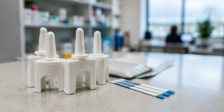 Close-up of naloxone nasal spray devices and drug test strips on a clinic counter in neutral daylight, illustrating the Los Angeles County opioid warning.