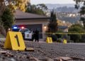Close-up of police evidence markers and a blurred residential hillside scene near Oakland’s Panoramic Hill, illustrating a fatal shooting investigation.