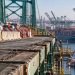 Close-up of the Vincent Thomas Bridge roadway and structural deck, with construction barriers and heavy port traffic blurred in the background.