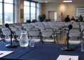 Community meeting room with a table of microphones in the foreground and rows of chairs blurred behind, illustrating a West Hollywood candidates forum.