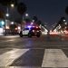 Crosswalk markings glow white in the immediate foreground of a nighttime Broadway street in Florence, with a patrol SUV blurred in the middle distance.
