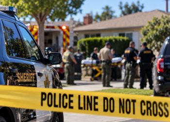Daytime law enforcement response outside a Bellflower residence, with a sheriff’s vehicle, emergency responders and investigators blurred behind police tape.