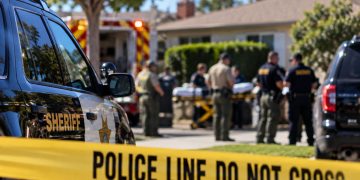 Daytime law enforcement response outside a Bellflower residence, with a sheriff’s vehicle, emergency responders and investigators blurred behind police tape.