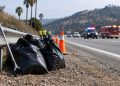 Daytime roadside embankment near Glendale with orange traffic cones, a litter grabber tool and filled trash bags in the foreground, hills blurred behind.