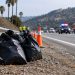 Daytime roadside embankment near Glendale with orange traffic cones, a litter grabber tool and filled trash bags in the foreground, hills blurred behind.