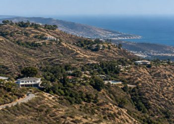 Dry chaparral hillside in the Santa Monica Mountains above Malibu in neutral daylight, with scattered homes along a winding canyon road.
