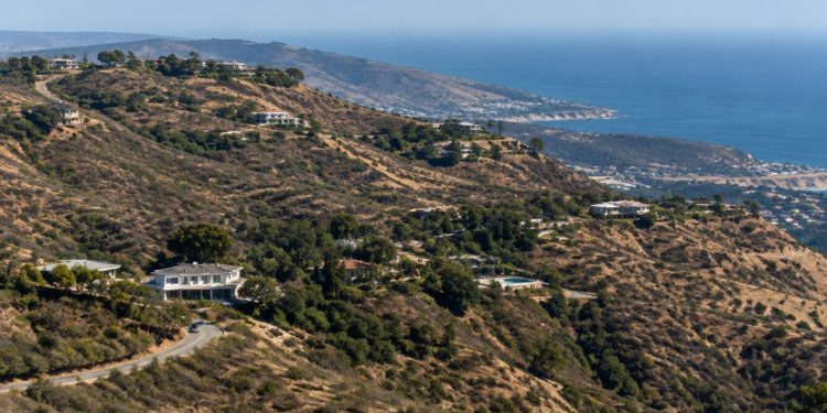 Dry chaparral hillside in the Santa Monica Mountains above Malibu in neutral daylight, with scattered homes along a winding canyon road.