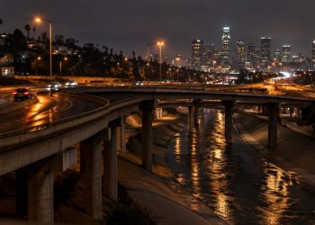 Elevated freeway ramps curving over the Los Angeles River channel in Cypress Park at night, with light trails from passing cars under street lamps.