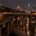 Elevated freeway ramps curving over the Los Angeles River channel in Cypress Park at night, with light trails from passing cars under street lamps.