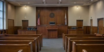 Empty courtroom with a wooden judge's bench, witness stand and rows of gallery seats under soft overhead light, illustrating the Superior Court judge race.