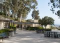Empty courtyard of a hillside school campus in Brentwood with low stucco buildings, a covered walkway and eucalyptus trees in afternoon daylight.