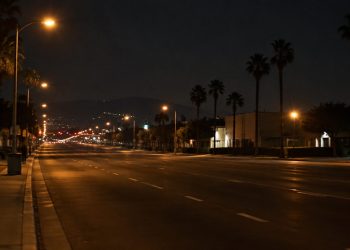 Empty multi-lane boulevard in the San Fernando Valley at night under street lamps, with low-rise buildings and palm trees along both sides.