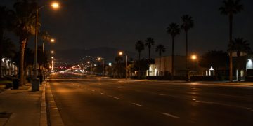Empty multi-lane boulevard in the San Fernando Valley at night under street lamps, with low-rise buildings and palm trees along both sides.