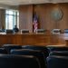 Empty wooden dais with high-backed leather chairs and microphones in a county government hearing chamber, illustrating the Los Angeles County Measure A vote.