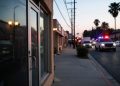Evening street in Florence-Graham with a closed business entrance in the foreground and emergency vehicle lights blurred far in the background.