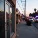 Evening street in Florence-Graham with a closed business entrance in the foreground and emergency vehicle lights blurred far in the background.
