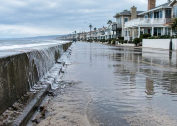High tide water pooling on a low-lying beachfront street lined with two-story beach homes in Newport Beach in neutral daylight.