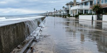 High tide water pooling on a low-lying beachfront street lined with two-story beach homes in Newport Beach in neutral daylight.
