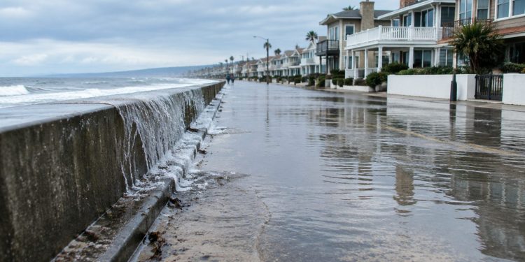 High tide water pooling on a low-lying beachfront street lined with two-story beach homes in Newport Beach in neutral daylight.