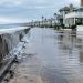 High tide water pooling on a low-lying beachfront street lined with two-story beach homes in Newport Beach in neutral daylight.