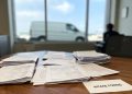 Illegible legal documents and intake forms in sharp focus on a wooden office desk, with blurred window light, office walls, and furniture in the background.