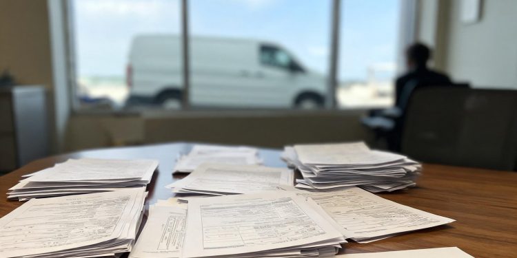 Illegible legal documents and intake forms in sharp focus on a wooden office desk, with blurred window light, office walls, and furniture in the background.