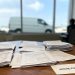 Illegible legal documents and intake forms in sharp focus on a wooden office desk, with blurred window light, office walls, and furniture in the background.