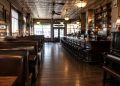 Interior of a historic downtown Los Angeles bar and restaurant with dark wood booths, vintage tin ceiling tiles and a piano in warm light.