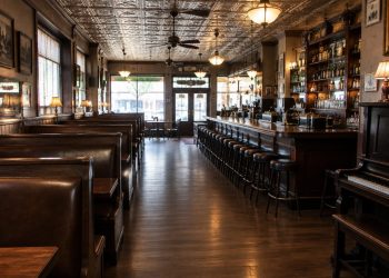 Interior of a historic downtown Los Angeles bar and restaurant with dark wood booths, vintage tin ceiling tiles and a piano in warm light.