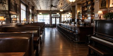 Interior of a historic downtown Los Angeles bar and restaurant with dark wood booths, vintage tin ceiling tiles and a piano in warm light.