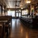 Interior of a historic downtown Los Angeles bar and restaurant with dark wood booths, vintage tin ceiling tiles and a piano in warm light.