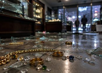 Jewelry chains and rings scattered among shattered glass on the floor of a dim jewelry shop interior, illustrating a Downtown Los Angeles burglary.