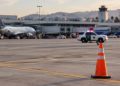 Late-afternoon view of an airport apron at John Wayne Airport with a traffic cone in the foreground and a patrol SUV blurred in the distance.
