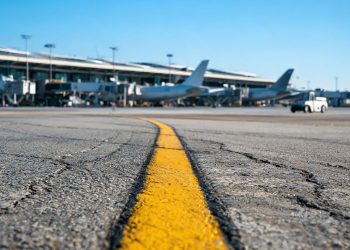 Late-morning view of a taxiway centerline at Los Angeles International Airport, with wide-body jets and terminal gates blurred in the background.