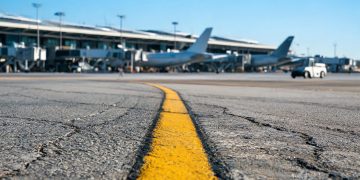Late-morning view of a taxiway centerline at Los Angeles International Airport, with wide-body jets and terminal gates blurred in the background.