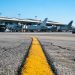 Late-morning view of a taxiway centerline at Los Angeles International Airport, with wide-body jets and terminal gates blurred in the background.
