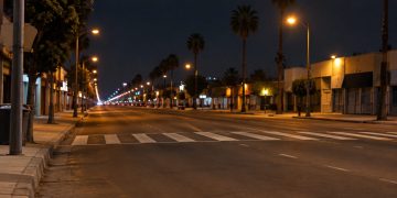 Long-lens night view of Central Avenue in South Los Angeles, with a crosswalk across empty lanes and low-rise buildings under street lamps.