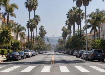 Long-lens view down Fountain Avenue in West Hollywood with parked cars along the curbs, a painted crosswalk, palm trees and low-rise apartment buildings in daylight.