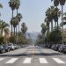 Long-lens view down Fountain Avenue in West Hollywood with parked cars along the curbs, a painted crosswalk, palm trees and low-rise apartment buildings in daylight.