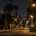 Long-lens view down North Fairfax Avenue in West Hollywood at night, with low-rise apartment buildings, palm trees and a parked sedan under street lamps.
