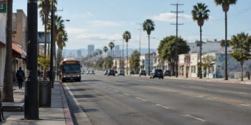Long-lens view down Vermont Avenue in South Los Angeles in morning daylight, with a city bus in the curb lane and palm trees along the street.