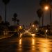 Long-lens view down a quiet residential street of stucco homes and apartment buildings with palm trees under street lamps at night in Santa Ana.