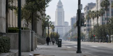 Long-lens view down an emptied Spring Street in downtown Los Angeles toward City Hall in afternoon daylight, with scattered litter on the sidewalk.