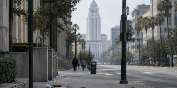 Long-lens view down an emptied Spring Street in downtown Los Angeles toward City Hall in afternoon daylight, with scattered litter on the sidewalk.
