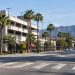 Long-lens view of a commercial street in downtown Burbank with a multilevel parking structure, low-rise storefronts and palm trees in afternoon daylight.