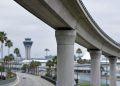 Long-lens view of an empty elevated concrete guideway curving above an access road at Los Angeles International Airport in neutral daylight.