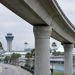 Long-lens view of an empty elevated concrete guideway curving above an access road at Los Angeles International Airport in neutral daylight.