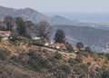 Long-lens view of dry chaparral slopes and hillside homes along a ridge in the Santa Monica Mountains of Los Angeles in neutral daylight.