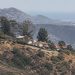 Long-lens view of dry chaparral slopes and hillside homes along a ridge in the Santa Monica Mountains of Los Angeles in neutral daylight.